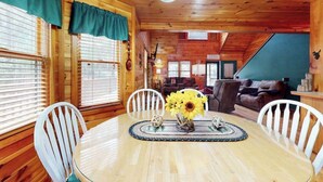 A wooden cabin interior with a dining table, white chairs, a sofa, and a staircase. - Our Mountain Blessing (Blairsville)