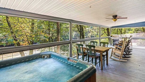 Ein Whirlpool auf einer Holzterrasse mit Blick auf Bäume, ein Tisch mit Stühlen und ein Deckenventilator.