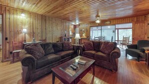 Ein Zimmer mit Holzwänden, einer Eckcouch, einem Couchtisch und einem Essbereich mit Stühlen.