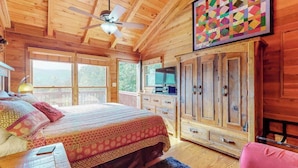 Ein Schlafzimmer in einer Holzhütte mit Bett, Kommode, Fernseher und Deckenventilator.