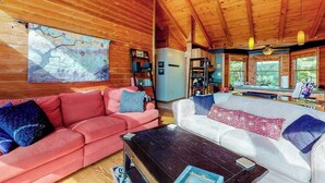 Ein gemütliches Blockhaus-Interieur mit Holzwänden, einem rosa-weißen Sofa, einem Couchtisch und einem Bild an der Wand.