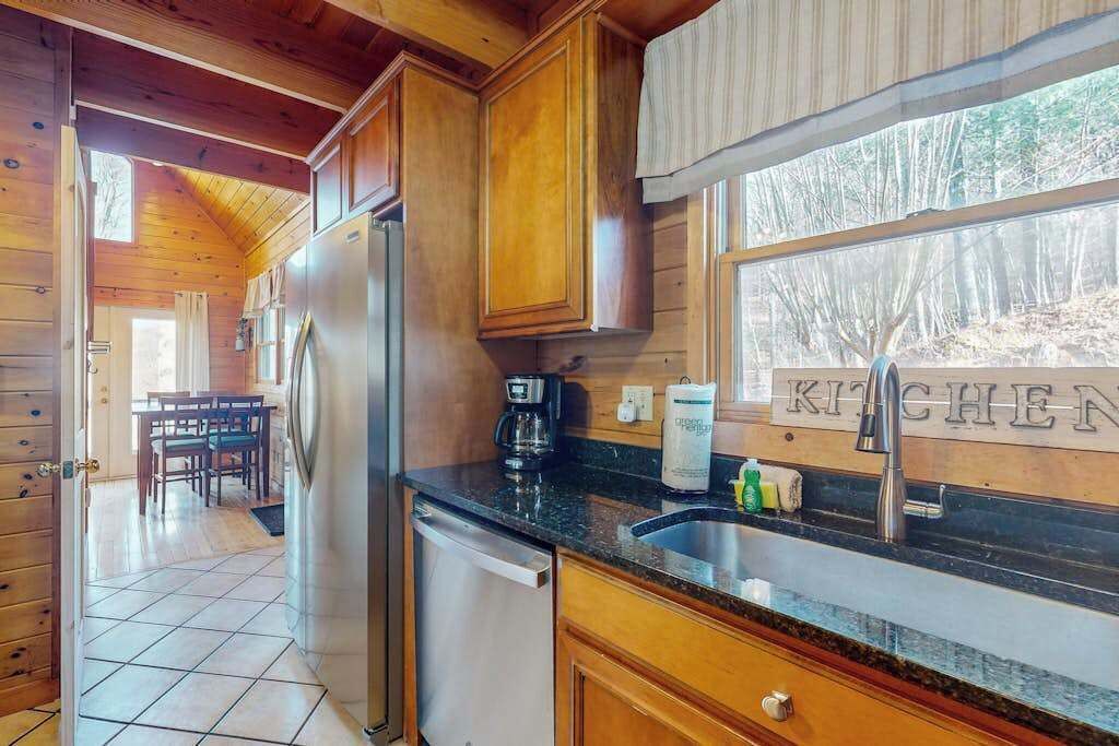 A wooden cabin kitchen with a refrigerator, coffee maker, and a window with a view of trees.