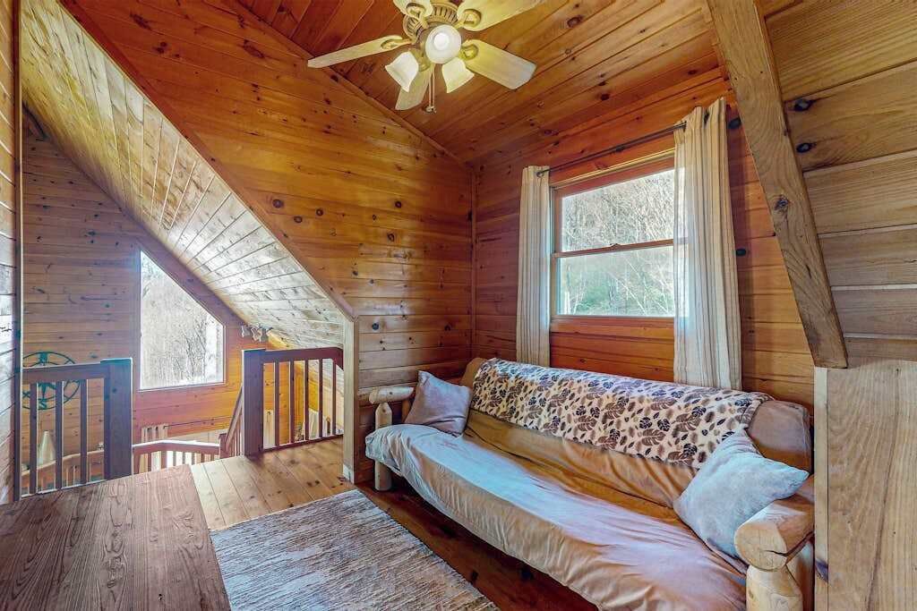 Una cabana acollidora amb interior de fusta, un ventilador de sostre, un sofà i una finestra amb cortines.