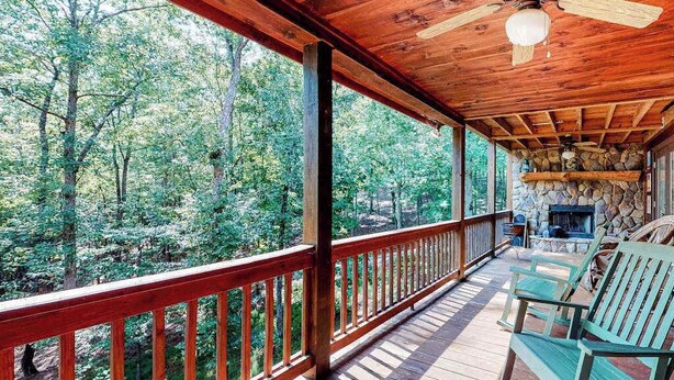 Eine Holzterrasse mit Kamin aus Stein, einem Deckenventilator und Blick auf den Wald.