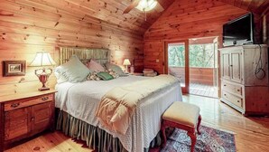 Ein Schlafzimmer in einer Holzhütte mit Bett, Nachttischen, einem Fernseher und Blick ins Freie.