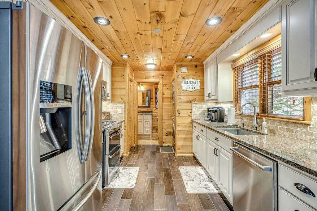 Cocina pequeña con paredes de madera, electrodomésticos de acero inoxidable y un cartel anunciando el desayuno.