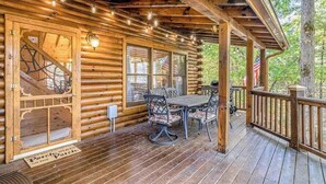 Een houten blokhut met een overdekte veranda, een eettafel met stoelen en uitzicht op het omliggende bos.
