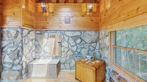 A cabin interior with wooden walls, a stone wall, a window with blinds, a basket, a wooden box, and two wall-mounted lanterns. - Time Out Blue Ridge - Hot tub (Blue Ridge)