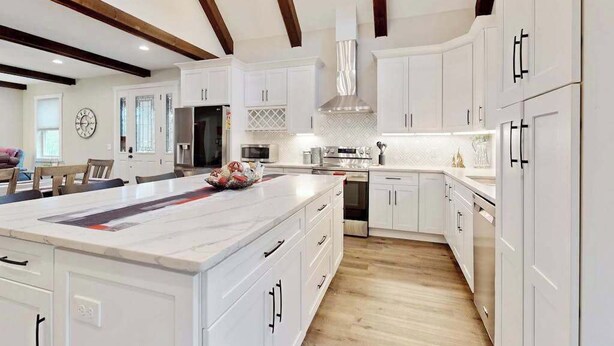 Une cuisine moderne avec des meubles blancs, un grand îlot central et un plafond en bois.