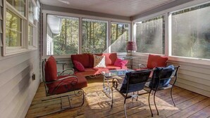 Une véranda avec un canapé rouge, une table basse en verre et des chaises en métal.