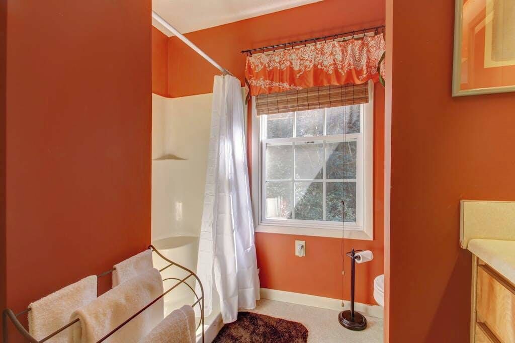 Ein Badezimmer mit Fenster, Duschvorhang, Handtuchhalter und Toilette.