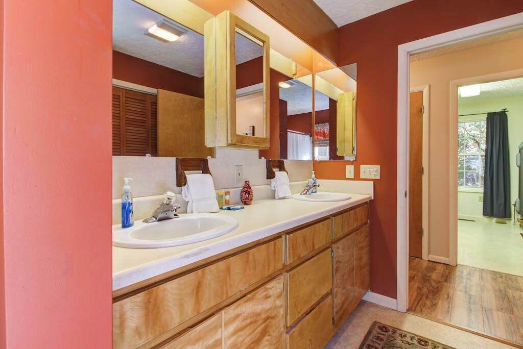 Ein Badezimmer mit zwei Waschbecken, einem großen Spiegel, Holzschränken und einer Tür zu einem anderen Raum.