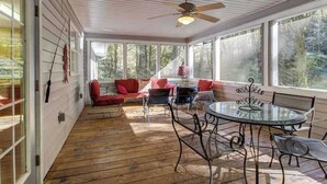 Une véranda avec une table et des chaises en verre, des chaises rouges et bleues, et un ventilateur de plafond.
