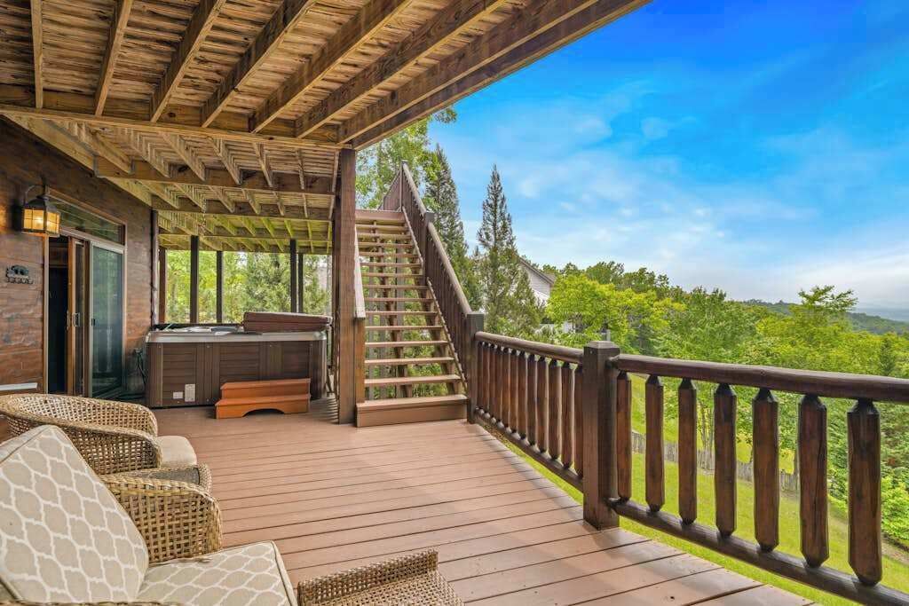 A wooden deck with outdoor seating, a hot tub, and a staircase leading to a balcony with a scenic view.