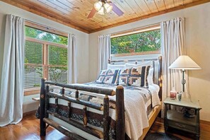 A bedroom with a wooden bed, two windows with curtains, a ceiling fan, and a bedside table with a lamp. - Endless Views Retreat (Mineral Bluff)
