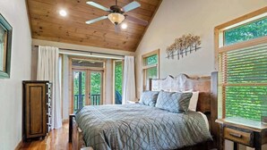 Ein Schlafzimmer mit Holzboden, einem Bett mit gesteppter Bettdecke, einem Nachttisch, einem Holzschrank und einem Fenster mit Jalousien.