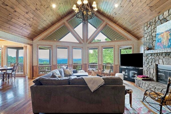 A spacious living room with a large sofa, a stone fireplace, and a television. - Endless Views Retreat (Mineral Bluff)
