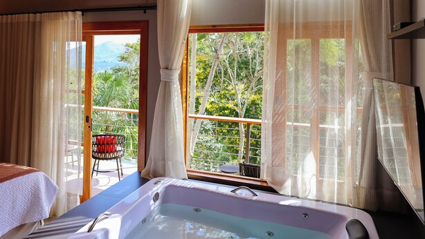 A spa room with a hot tub, large windows, and a view of greenery.