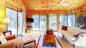 A log cabin interior with a sofa, armchair, wooden coffee table, and a television on a stand. - Life's a River Stays (Ellijay)