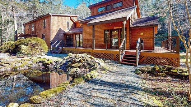 A cabin with a wooden exterior, a deck, and a small pond. - Life's a River Stays (Ellijay)