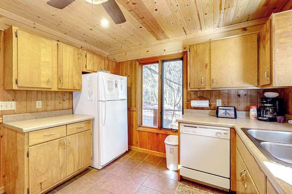A wooden cabin kitchen with cabinets, a refrigerator, a dishwasher, and a window.