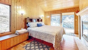 A wooden cabin bedroom with a bed, built-in shelves, a window, and a fireplace. - Life's a River Stays (Ellijay)
