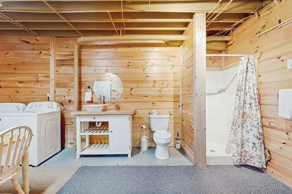 Une salle de bain compacte, aménagée avec des meubles en bois, comprenant une machine à laver, des toilettes et un espace douche.