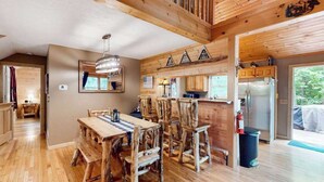 Un interior rústico de madera con una mesa de comedor, sillas, una zona de cocina y vistas al exterior.