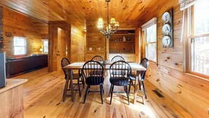 Interno di una baita in legno con tavolo da pranzo, sedie, un lampadario e angolo cottura.
