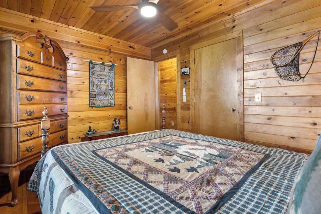 Camera da letto in una baita di legno, con un letto, una cassettiera e una ventola a soffitto.