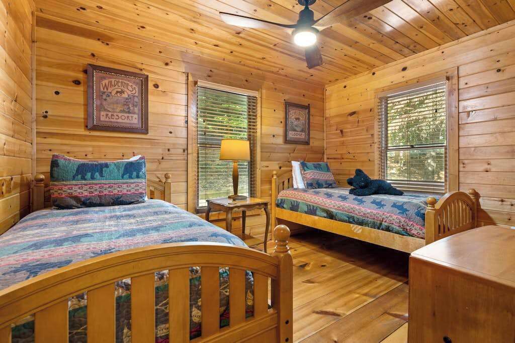 A cabin with two wooden beds, a ceiling fan, and framed pictures on the walls.
