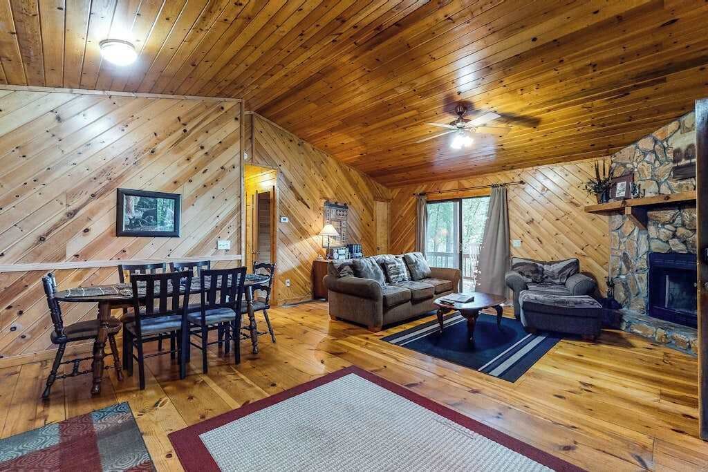A wooden cabin interior with a dining area, sofa, and fireplace.