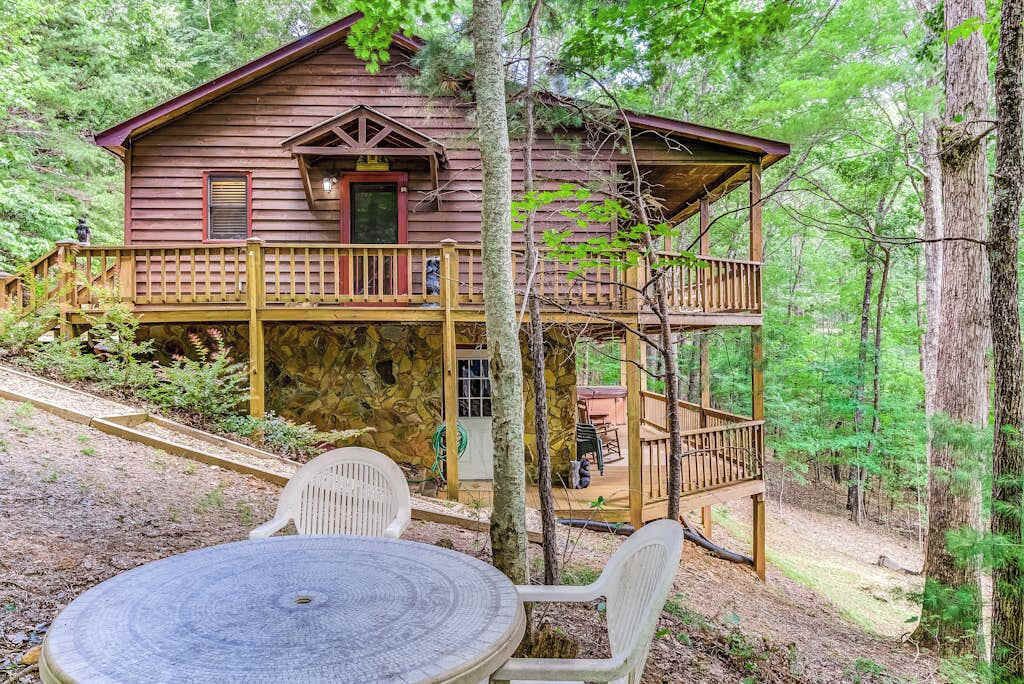 Eine Holzhütte mit einer zweistöckigen Veranda, einem Esstisch und Stühlen in einer Waldlandschaft.