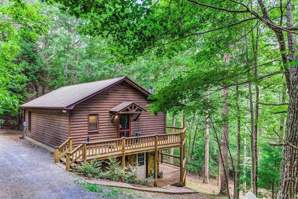 A wooden cabin with a porch, surrounded by dense forest.
