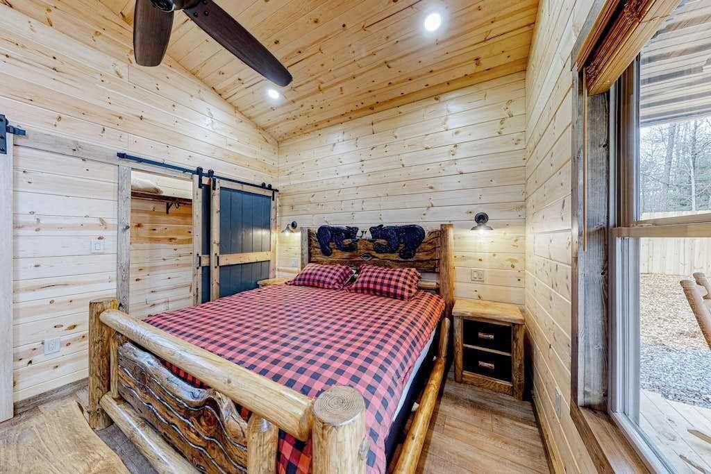 A wooden cabin bedroom with a bed, a ceiling fan, a window, and a door.