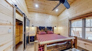 Un dormitori de cabana de fusta amb un llit, un ventilador de sostre, una finestra i una porta.