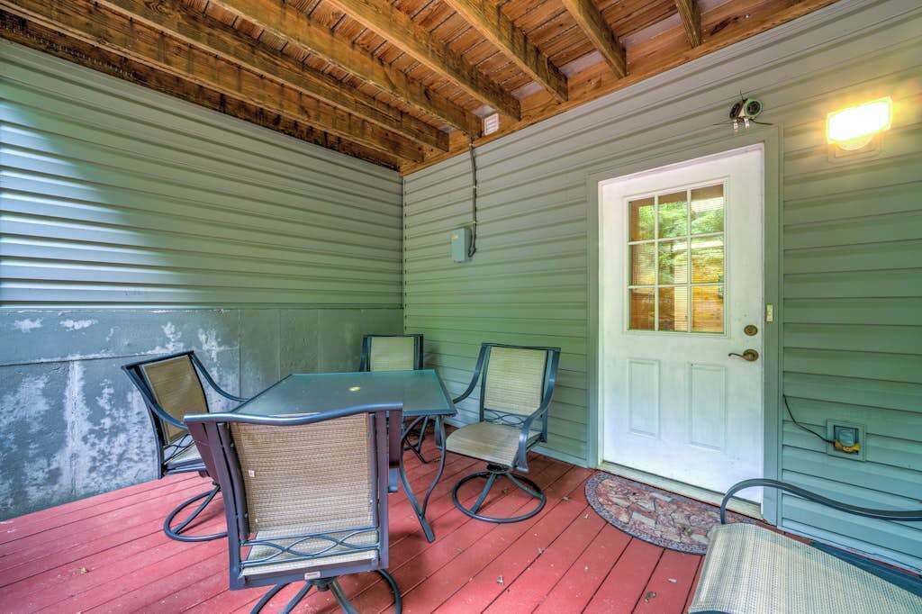A covered porch with a table and chairs, a door with a window, and a wooden ceiling.