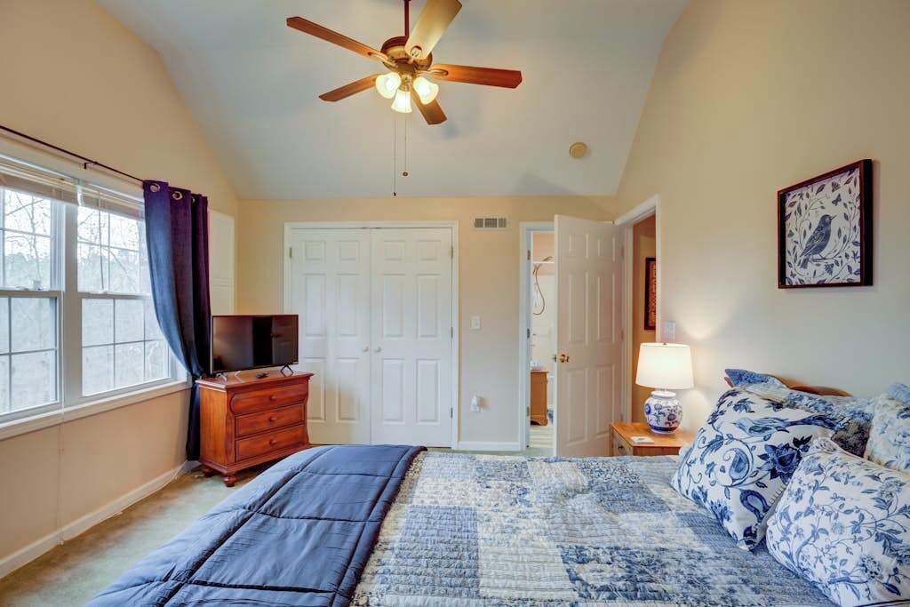 A bedroom with a bed, a ceiling fan, a dresser, a television, and a door leading to another room.