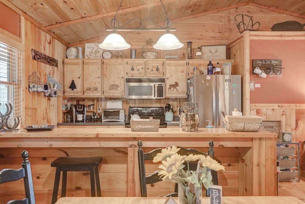Una cocina rústica con armarios de madera, una isla central, microondas, refrigerador y un comedor con una silla y mesa.