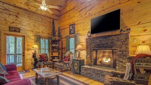 A log cabin interior with a stone fireplace, wooden walls, a flat-screen TV, and a cozy seating area. - Jack Bear's Cabin Stay (Blue Ridge)