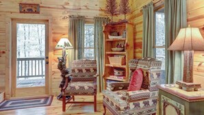 A log cabin interior with a fireplace, patterned chairs, a bookshelf, and a door leading outside. - Jack Bear's Cabin Stay (Blue Ridge)