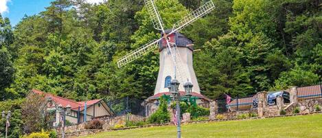 A windmill with a stone base, surrounded by a stone wall, and a small building with a red roof in the foreground.