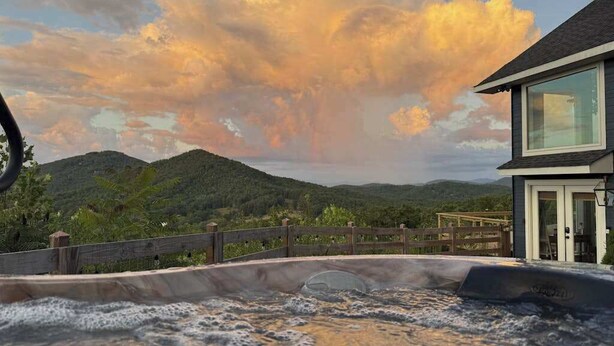 Ein Whirlpool mit einer Holterrasse, einem durchsichtigen Raum und einer Berglandschaft im Hintergrund.