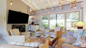 Un amplio salón con una televisión de pantalla plana, muebles de mimbre y ventanas grandes.