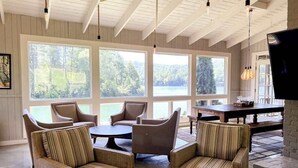 Una habitación con amplios ventanales, muebles de mimbre, una mesa de comedor y una televisión de pantalla plana.