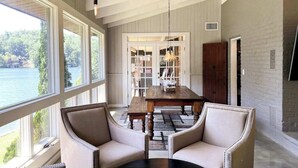 Una habitación con un ventanal grande, una mesa de madera, dos sillones tapizados y vistas a un lago.