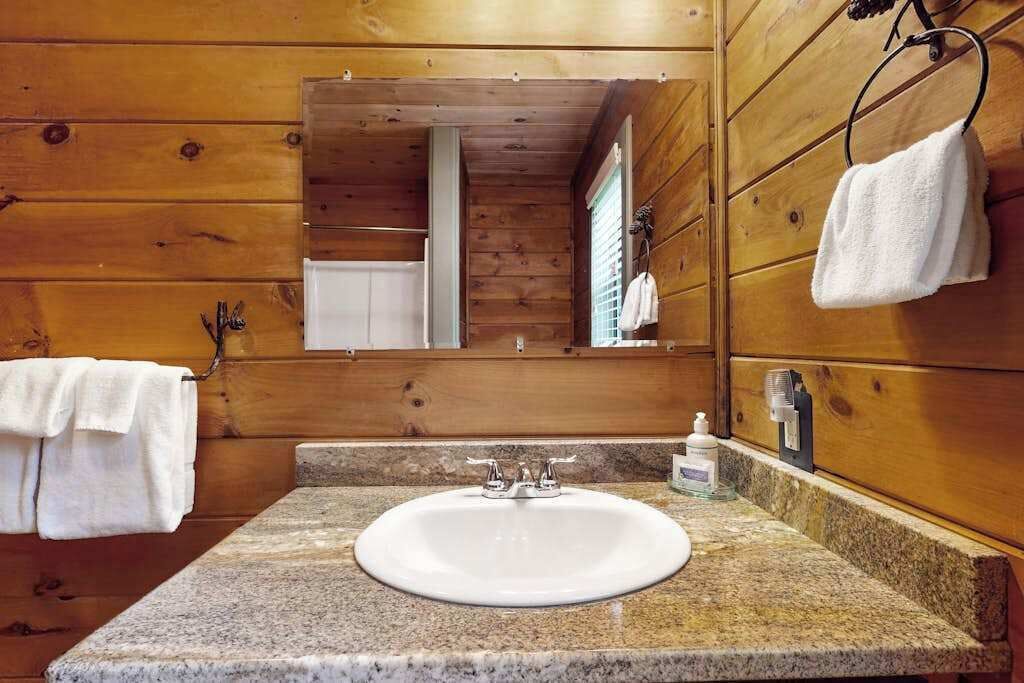 A wooden cabin bathroom with a granite countertop sink, a mirror, and a towel rack.