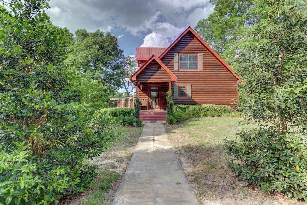 A wooden cabin with a stone pathway leading to the entrance, surrounded by lush greenery.