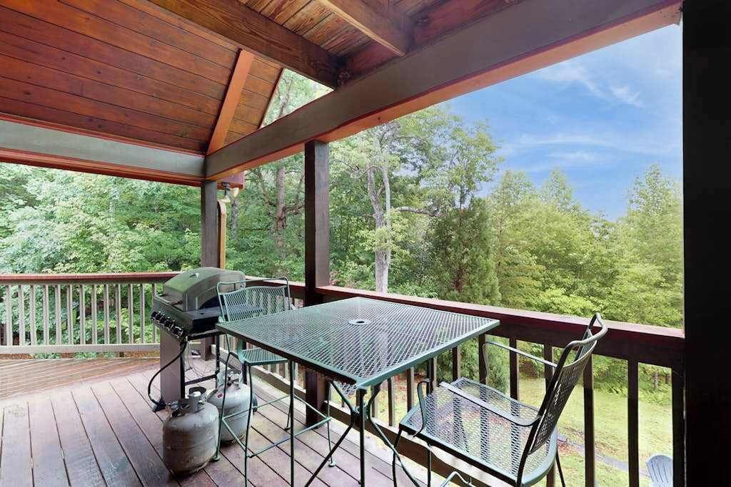 A covered outdoor deck with a grill, chairs, and a table.