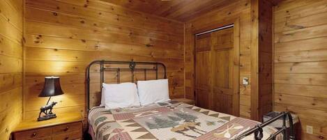 A wooden cabin bedroom with a bed, nightstand, lamp, and a ceiling fan.